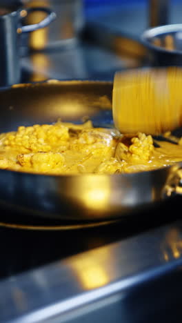 frying pan with seafood cooked in the cheese sauce. cook mixes the dish with wooden spatula. close up. vertical video.