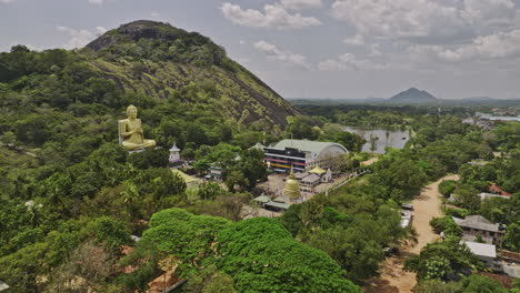 dambulla sri lanka aerial v1 low drone flyover uyanwaththa viharaya buddhist temple capturing golden lord buddha sculpture sitting in chakra pose by the hillside - shot with mavic 3 cine - april 2023