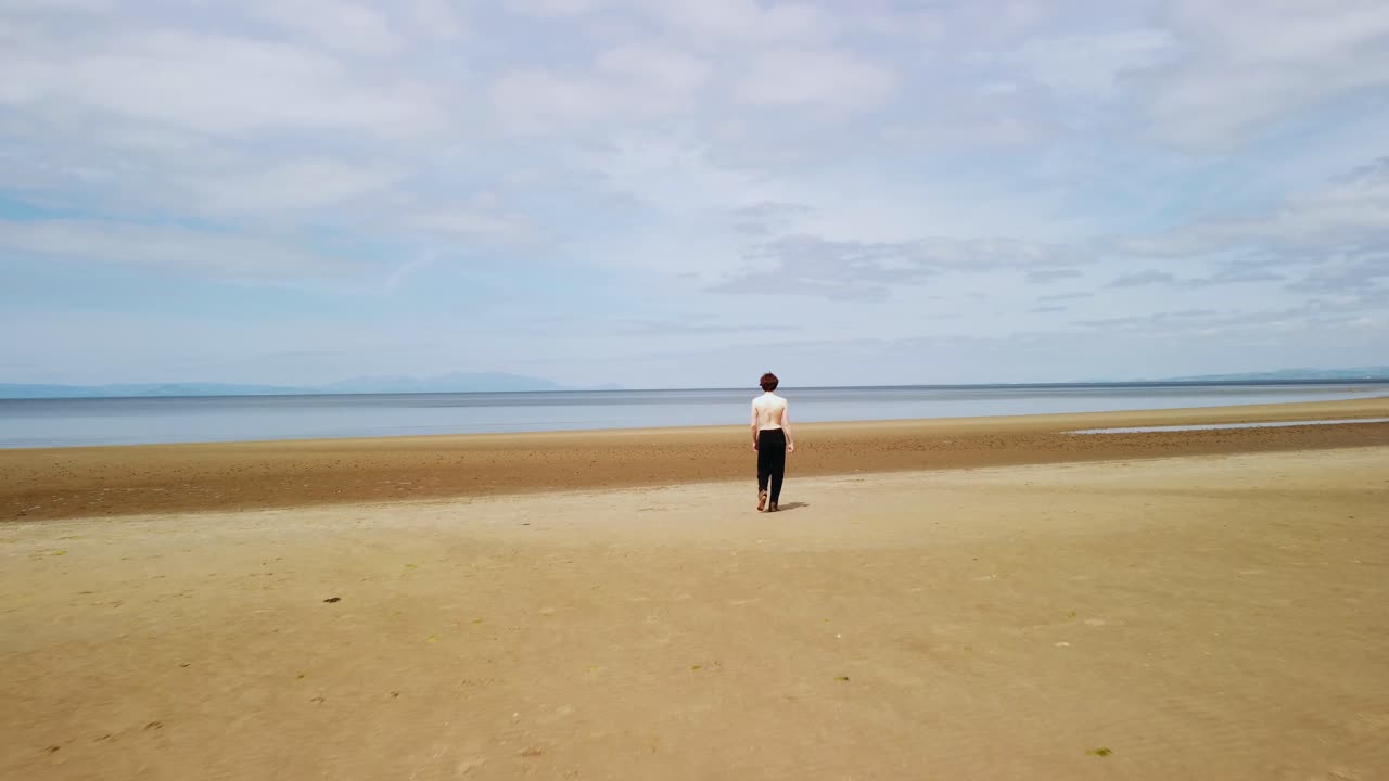 셔츠나 신발이 없는 젊은 남자가 바다를 향해 해변을  ⁇ 고 있습니다.