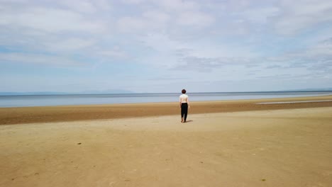 young man without a shirt or shoes walks on a beach towards the sea