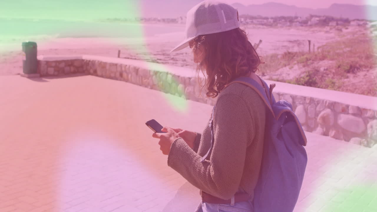 woman typing on smartphone at beach walkway, showing floating chat bubbles and finance charts