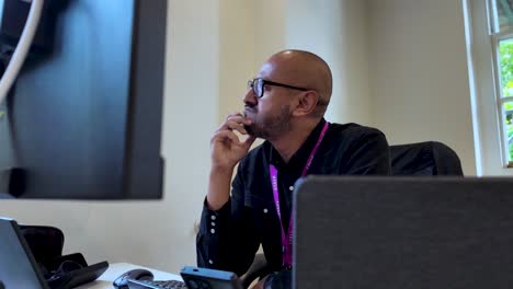 a man sits in front of a computer screen in an office setting, gazing thoughtfully into the distance, embodying the concepts of problem-solving and critical thinking