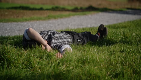 tired white man in flannel lays on grass calling dog and petting it at golden hour