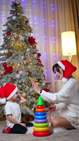 happy mom and son in red caps giving high five to each other. game time on the cozy evening near the christmas tree. vertical video.