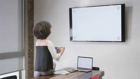mujer de negocios casual biracial haciendo una llamada de video usando tableta y monitor, espacio de copia, cámara lenta