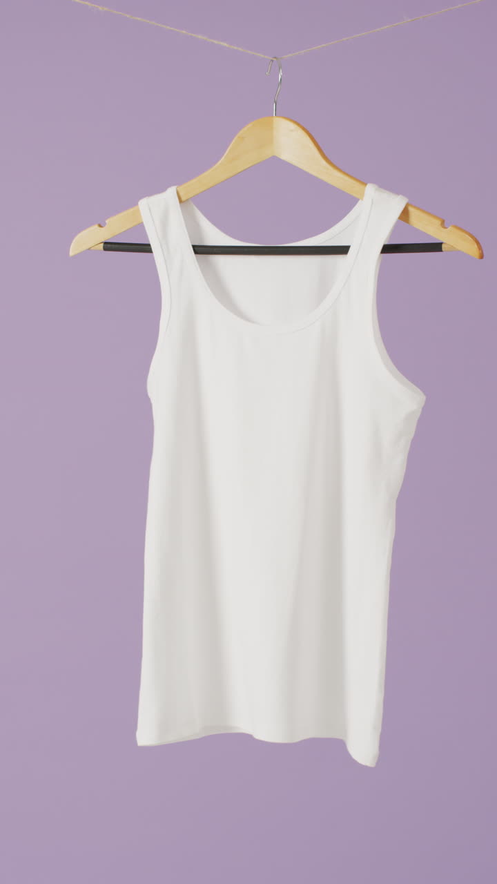 Vertical video of close up of white vest hanging on purple background with copy space