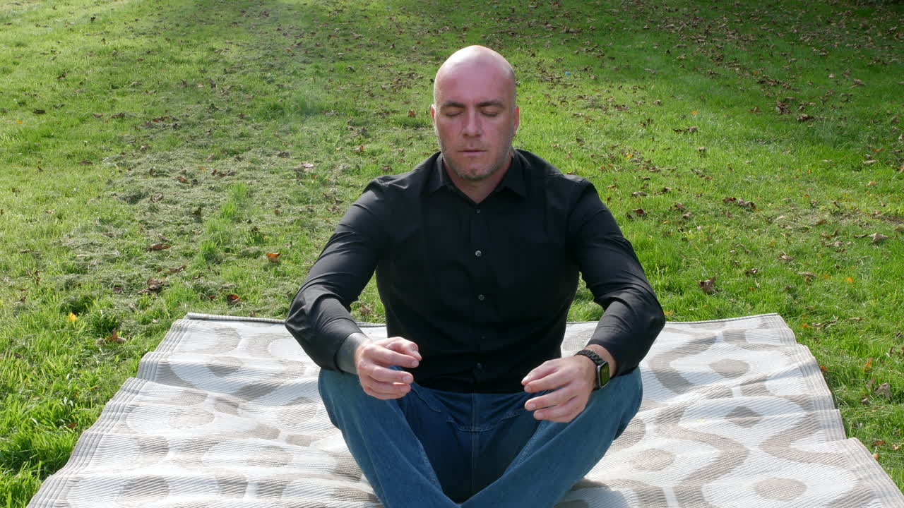 Un uomo che medita seduto su un tappetino in posizione yoga, praticando la consapevolezza all'aperto in meditazione