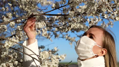 girl in white jacket photographs white color in spring using smartphone for photo blonde girl in a white mask makes a selfie on a background of flowering fruit trees photos for social networks