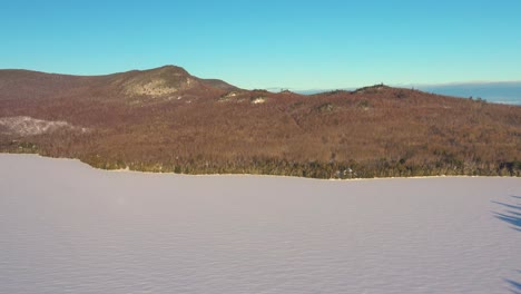 Tobogán-Aéreo-Sobre-Un-Lago-Congelado-Con-La-Orilla-Boscosa-Montañosa-En-La-Distancia