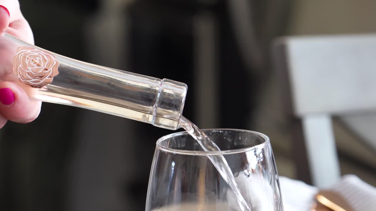 장미 와인은 사람들이 배경, 흰색, 황금색 붉은 색으로 걷고 있는 분홍색 매니큐어를 입은 여성이 와인 병 줄기에서 와인 잔에 천천히 부었습니다.