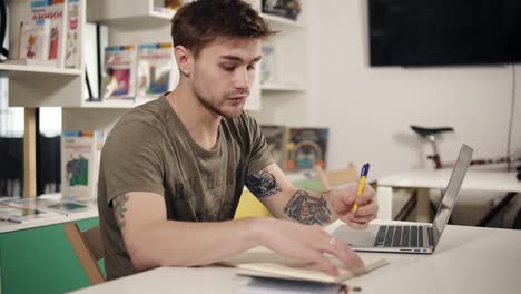 attractive young male programmer teacher writes something down in his notebook, looking very serious.