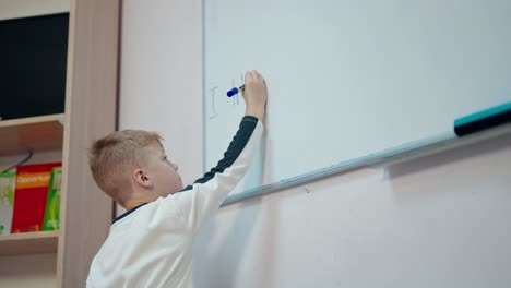 boy studying at school. schoolboy writing on a whiteboard with a marker in the classroom. elementary education.