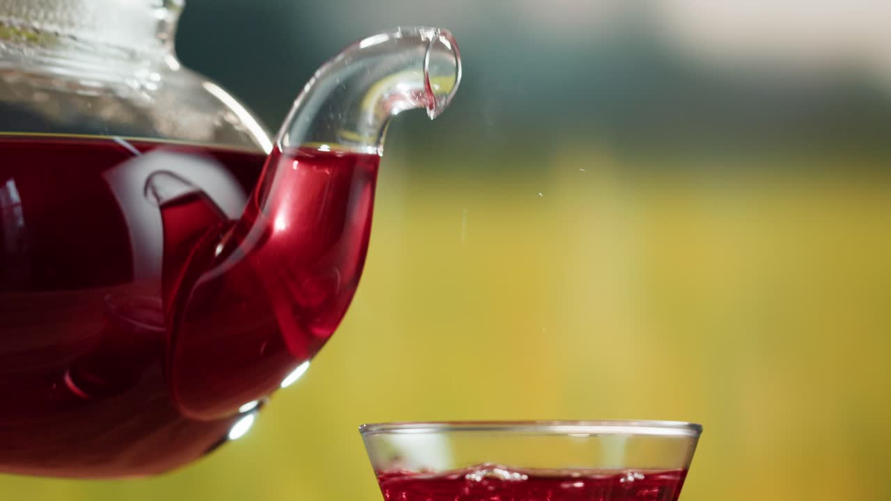 Pouring Red Herbal Tea from a Glass Teapot