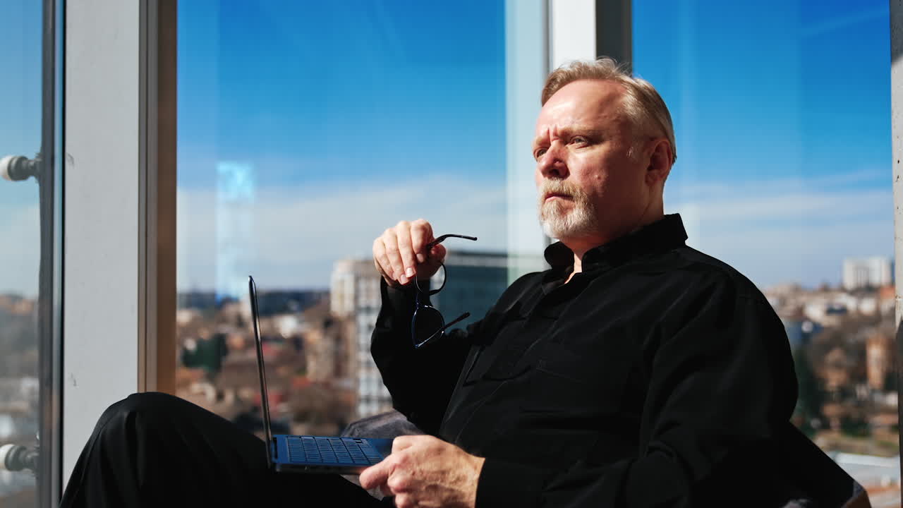 Mature Caucasian male looks attentively on the laptop. Pensive man puts off glasses and looks aside thinking over the issue. Close up.