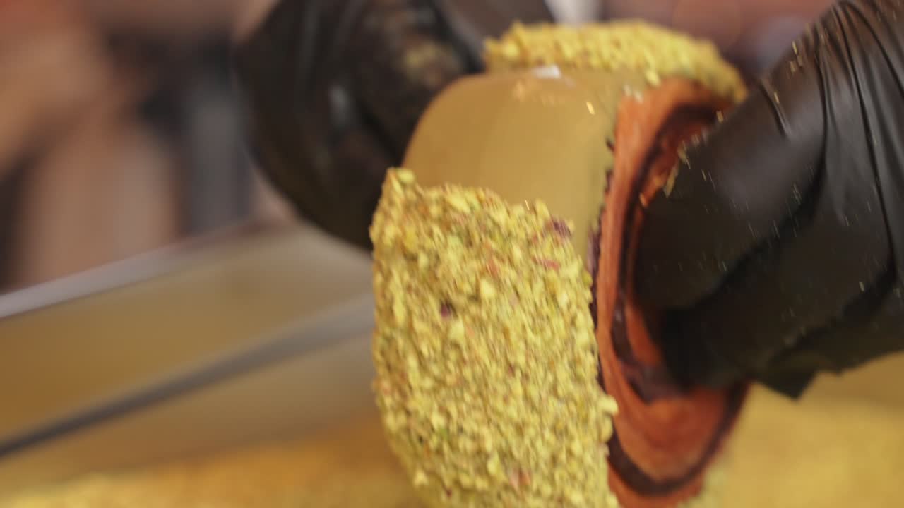 donut de croissant de pistacho siendo decorado rodando sobre crema y pistacho de cerca