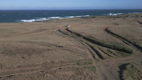 Aerial-follows-white-truck-on-rough-grass-road-toward-Mahana-Beach,-HI