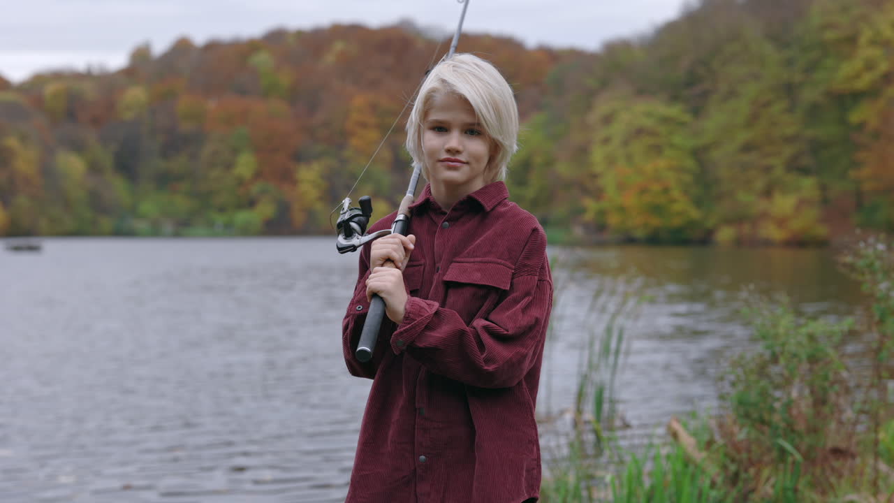 Young person holding a fishing rod by a lake in autumn