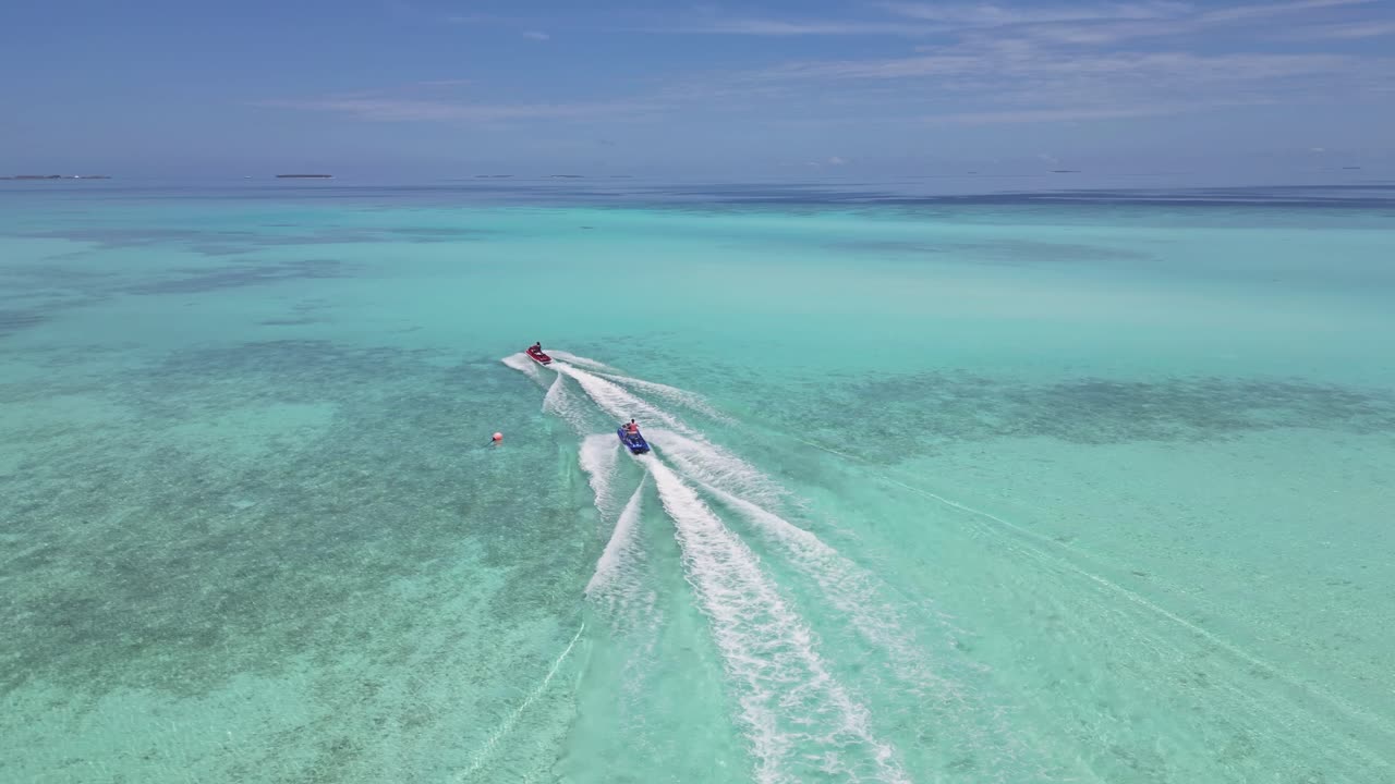 Couple on jet ski speeding over crystal clear water of Indian ocean at sunny day. Aerial tracking shot. Luxury island of Maldives in summer. Wide shot.