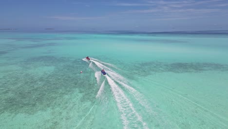 couple on jet ski speeding over crystal clear water of indian ocean at sunny day. aerial tracking shot. luxury island of maldives in summer. wide shot.