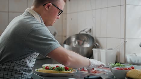 hombre caucásico con síndrome de down preparando un sándwich en una cocina comercial.