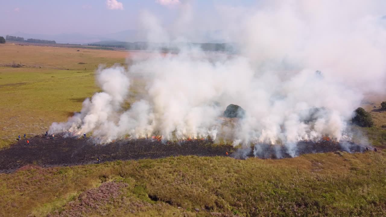 방대한 개방된 풍경에서 풀을 가로질러 불타는 통제된 화재의 연기가 아져 나옵니다.