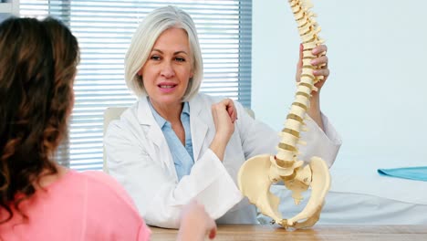 doctora explicando el modelo de la columna vertebral a una paciente