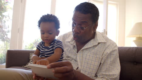 Grandfather-And-Grandson-Reading-Book-At-Home-Together