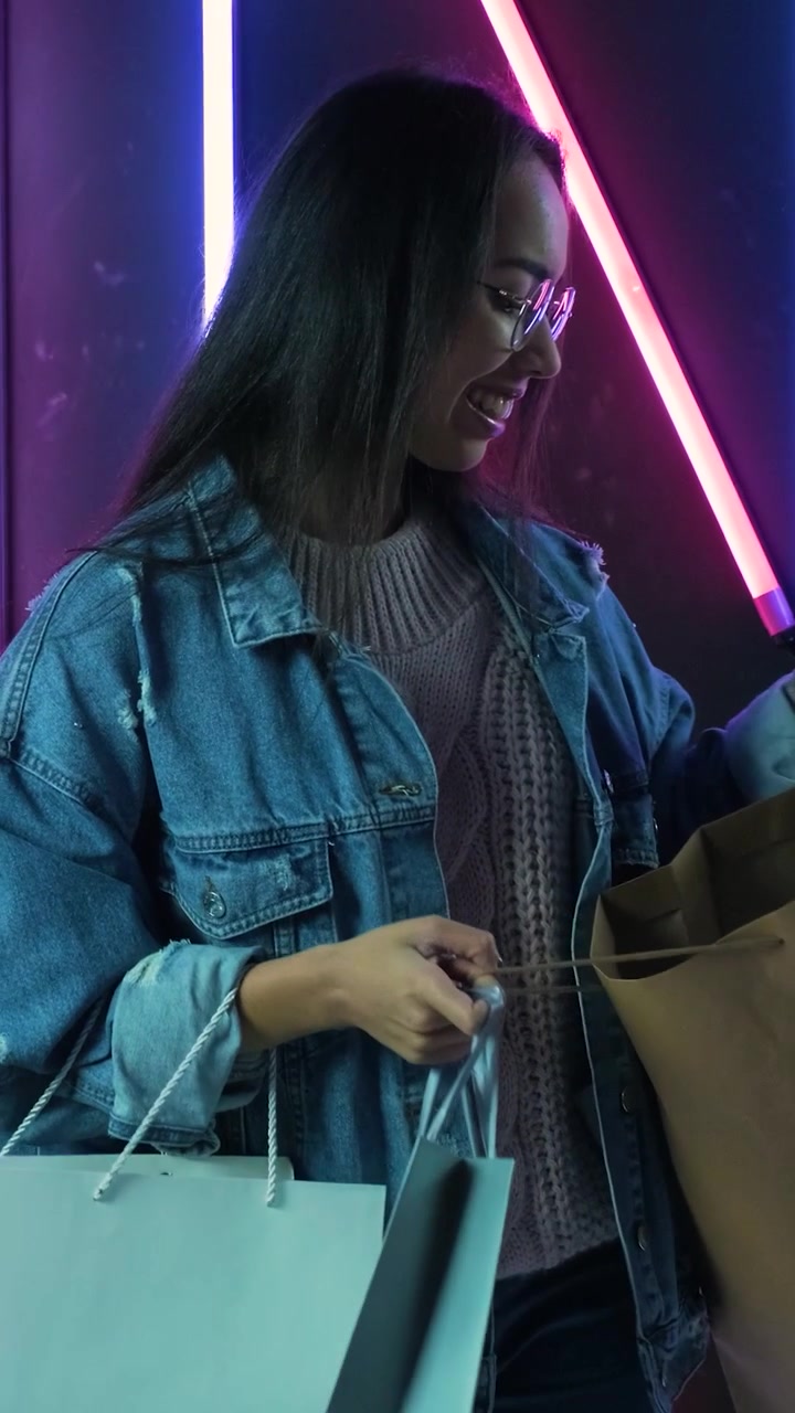 Giovane donna felice con borse della spesa in un negozio illuminato al neon