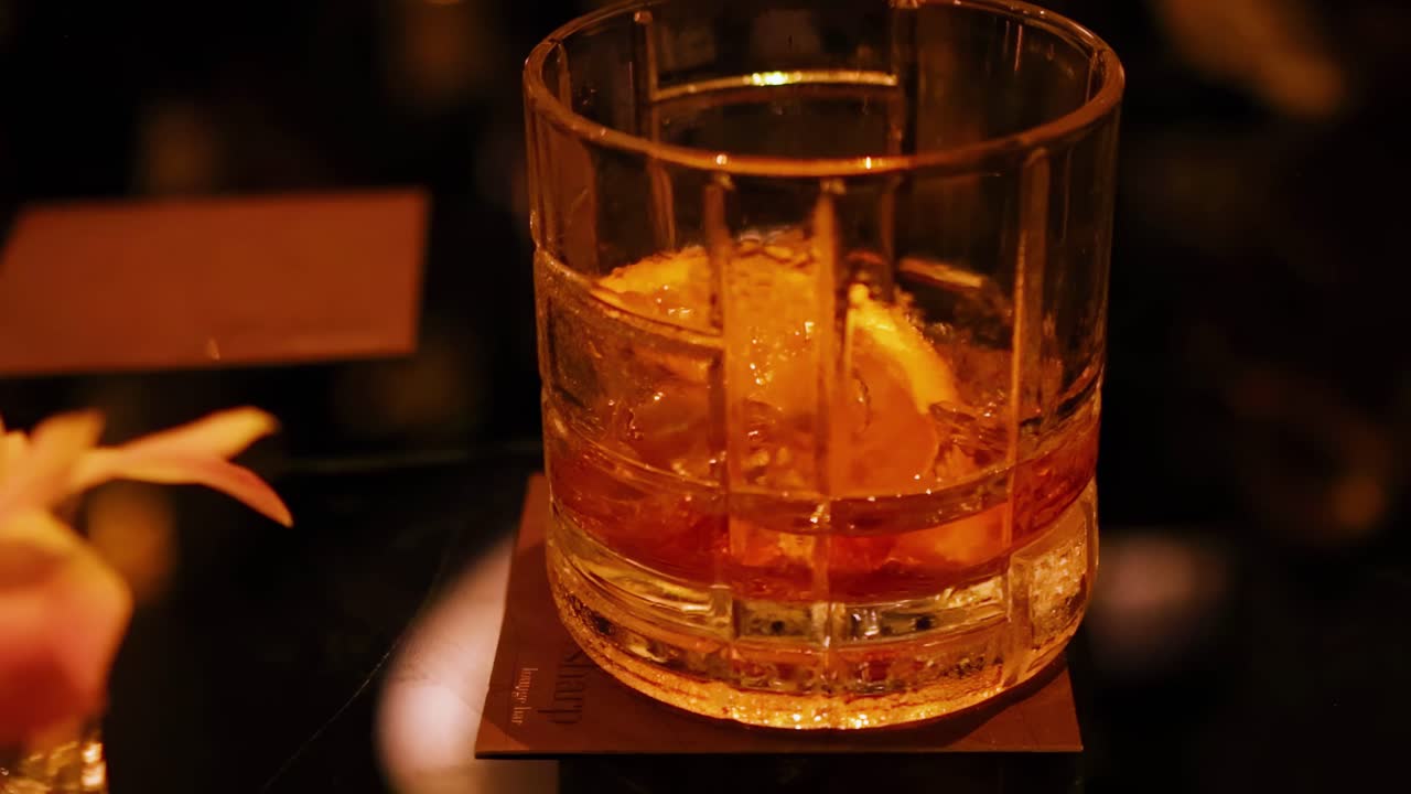 Close-up of a whisky glass with an orange slice on a dimly lit table.