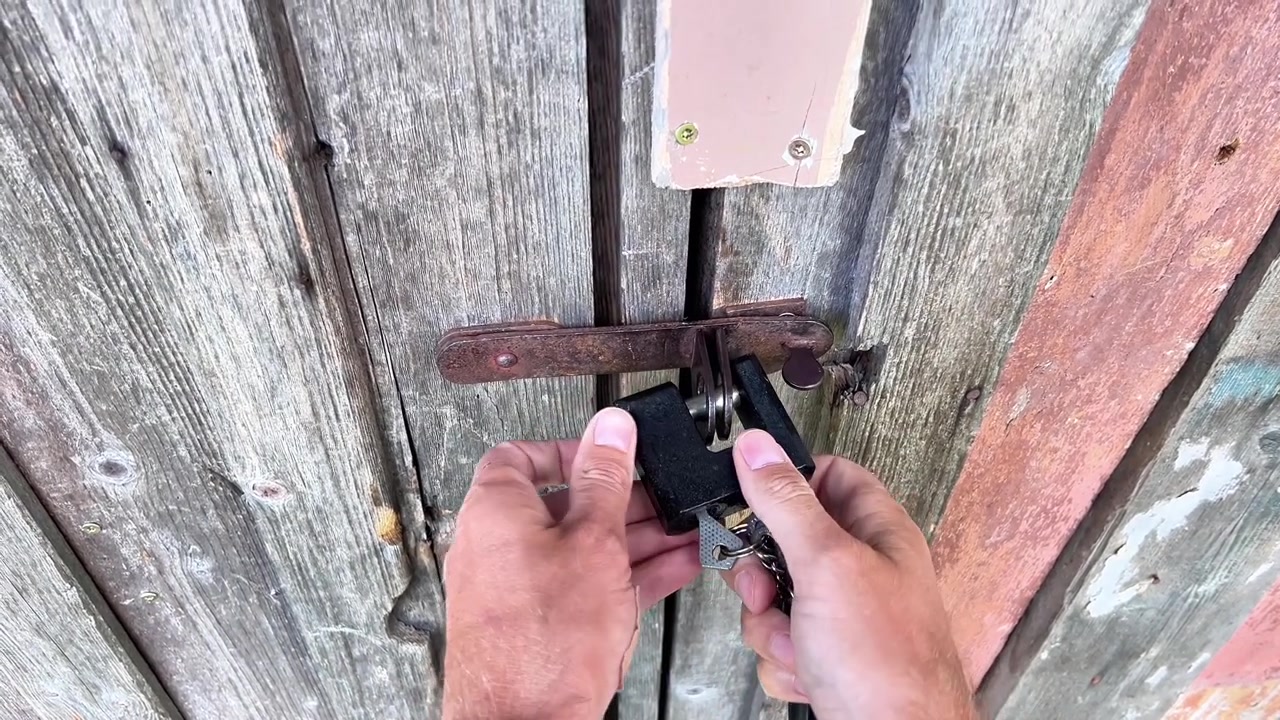 A person inserts a key to unlock a heavy padlock on an old wooden door. Ideal for security, real estate, privacy concepts, and property protection content.