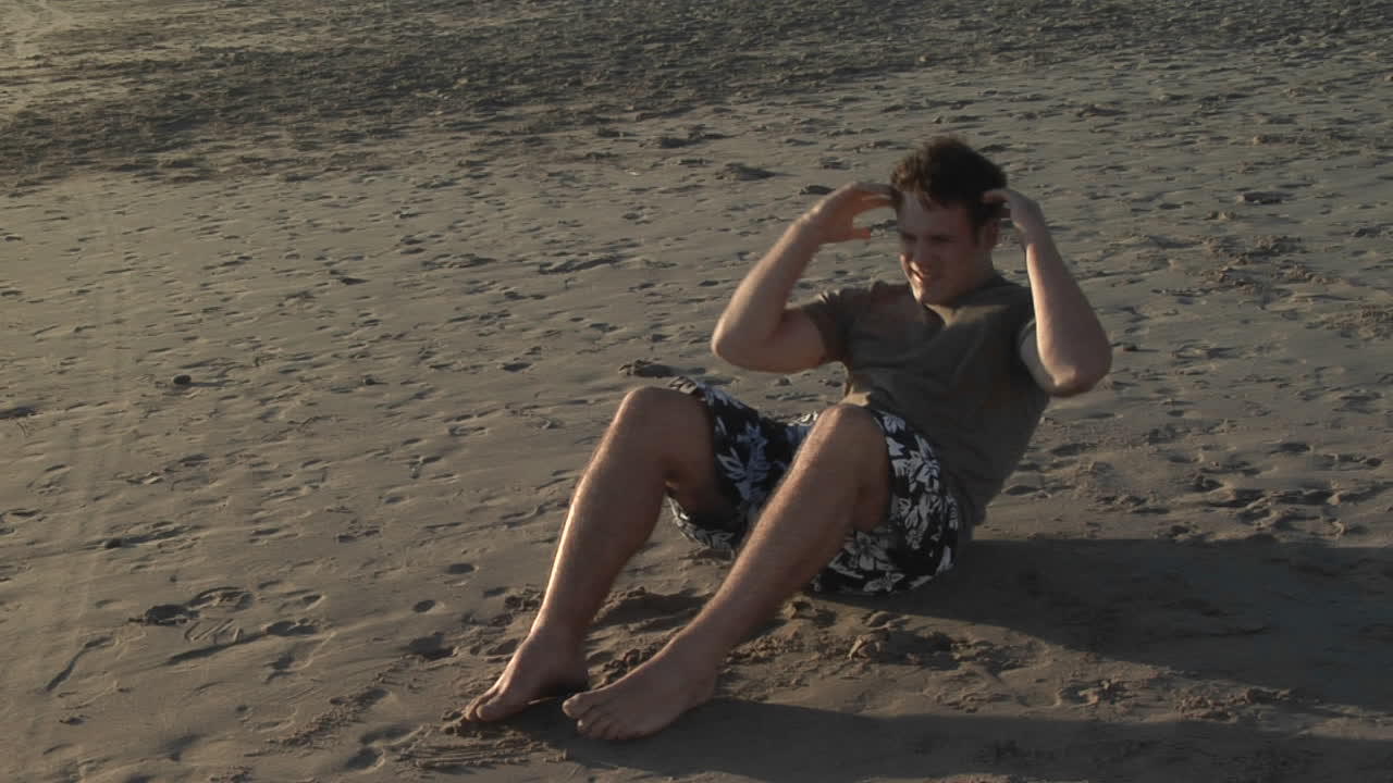 un hombre hace sentadillas en una playa de arena