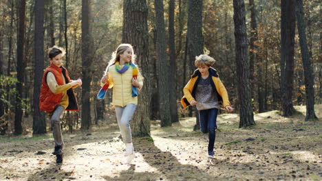 joyful kids, girl and two boys, running and having fun in the forest on a sunny day