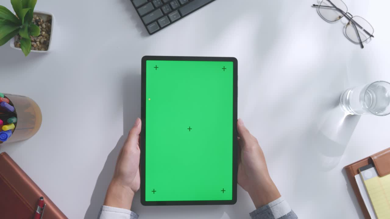 верхний вид ноутбука с макетным зеленым экраном chromakey на деревянном офисном столе рядом с ноутбуком с ручками, очками и стаканом воды.
