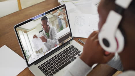 african american businessman sitting at desk using laptop having video call with male colleague