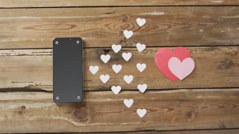 paper hearts and smartphone on wooden background at valentine's day