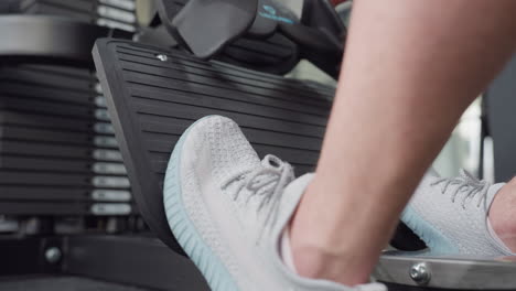 athlete places foot on weight machine pedal, leg tightening with powerful contraction as he pushes resistive load for leg workout in gym setting with visible muscle engagement and focused intensity