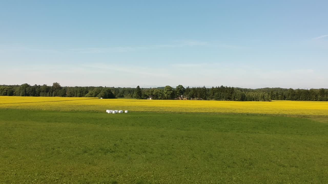 una toma aérea lateral cerca del suelo sobre un campo verde y amarillo con forraje envuelto en plástico blanco