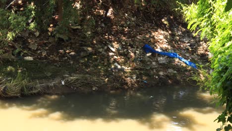 River-current-passing-by-destroyed-riverbank-with-non-biodegradable-garbage-and-affected-greenery-due-to-inundation-and-flooding