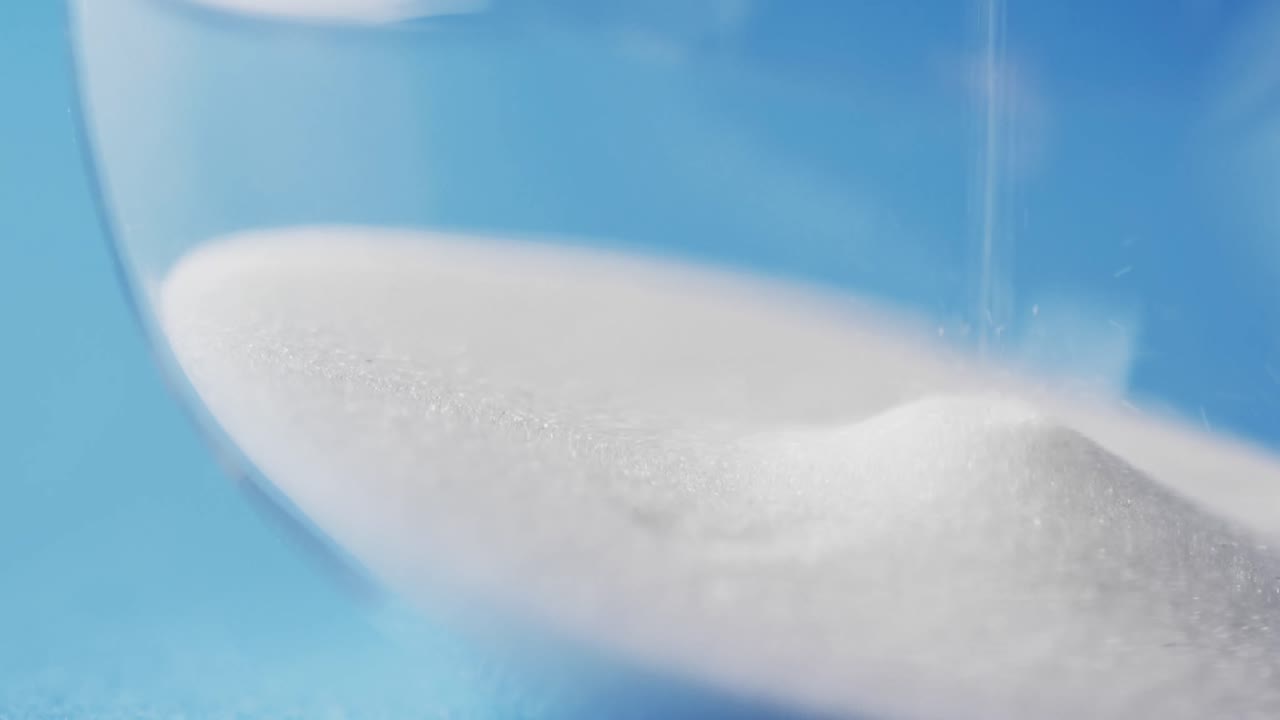 파란색 배경에 복사 공간과 함께  ⁇  모래를  ⁇ 는 모래시계의 클로즈업 비디오