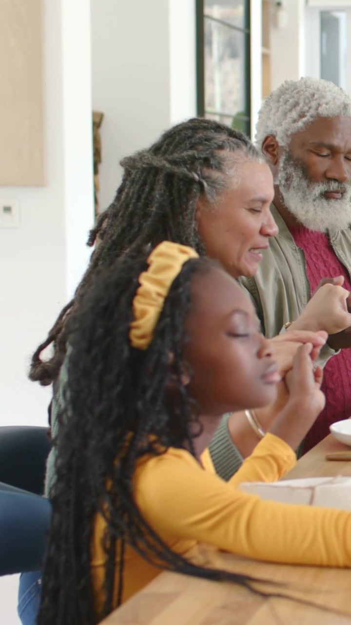 Vertical video: Closing eyes child joining elders at counter, meal arriving, headband, copy space