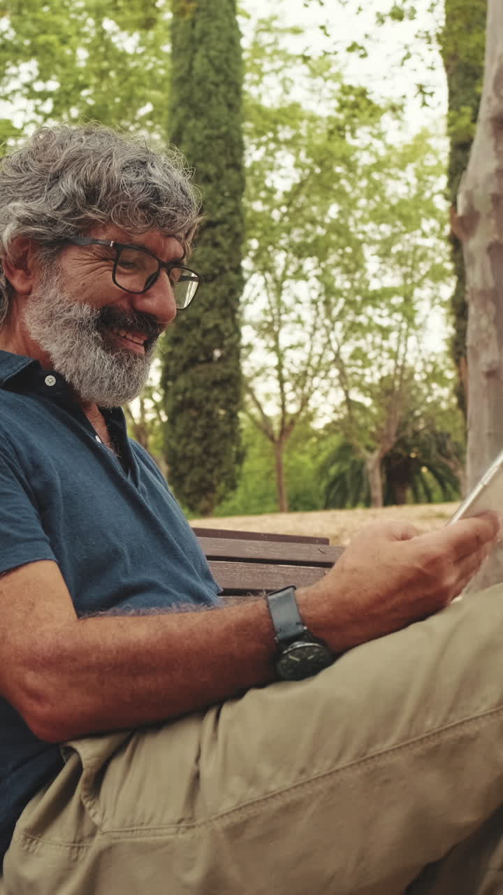 Hombre maduro sonriendo usando un smartphone en un banco del parque