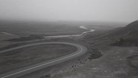 Drone-shots-of-skater-going-downhil-on-curvy-road-in-a-foggy,-dramatic-landscape-in-Iceland