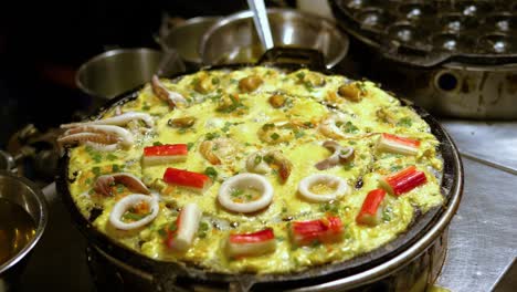 Traditional-seafood-omelet-on-an-flat-grill-street-food-market,-Bangkok