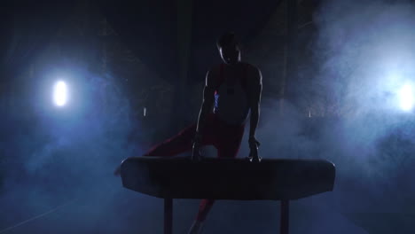 male gymnast performs pommel horse exercise in a dark room in smoke in slow motion. sports for health and achievement