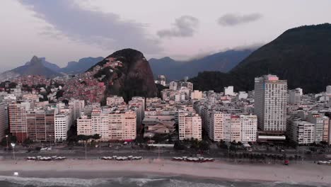 Movimiento-Aéreo-Hacia-Atrás-Que-Muestra-El-Barrio-De-Copacabana-En-Río-De-Janeiro-Temprano-En-La-Mañana-Revelando-La-Playa-Y-El-Bulevar-En-Primer-Plano-Y-El-Horizonte-De-La-Ciudad-En-El-Fondo