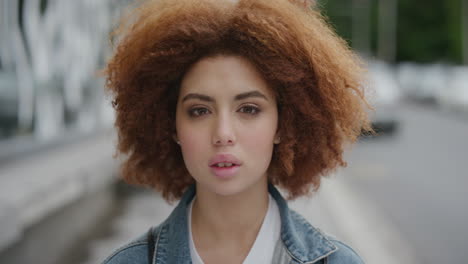 retrato de una linda mujer joven de raza mixta mirando a la cámara pensativa tranquila hermosa estudiante femenina roja afro peinado rizado en la calle de la ciudad urbana serie de personas reales
