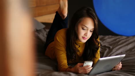 Woman-using-digital-tablet-and-mobile-phone-on-bed