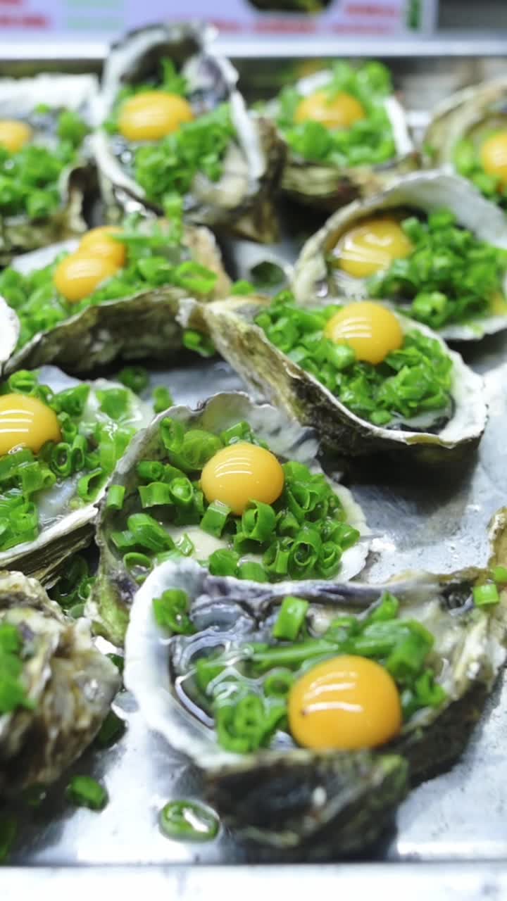 Vertical screen Oysters With Egg Yolk And Scallions Glistening In Shell, Closeup Seafood Display On Stainless Tray At Vietnamese Street Market, Bright Orange Yolk And Chopped Green Onion,