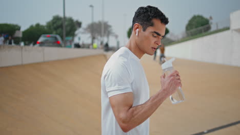 muscular athlete drinking bottle outdoors. professional runner resting refresh