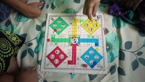 asian indian family playing ludo board game on bed at home, female hand rolling dice top down view, slow motion